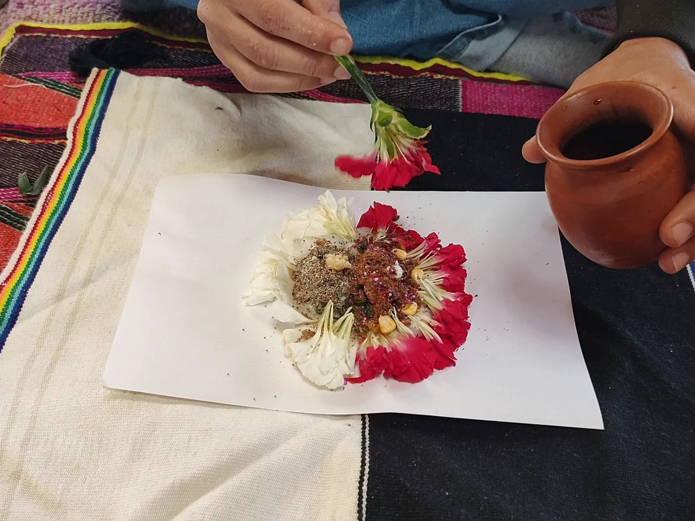 Preparación de un despacho andino sobre tejidos, con flores, hojas y recipientes.