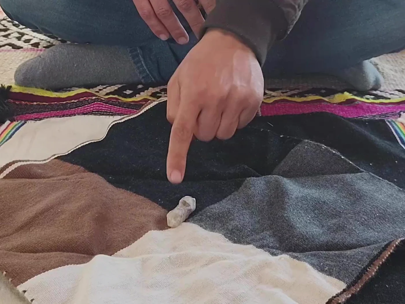 Missa andina doblada y sostenida por una watana, entre pétalos y hojas.